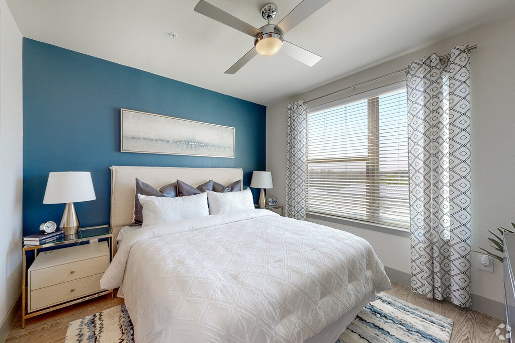 Ironcrest model bedroom with a large white bed and blue walls and large windows  and ceiling fan