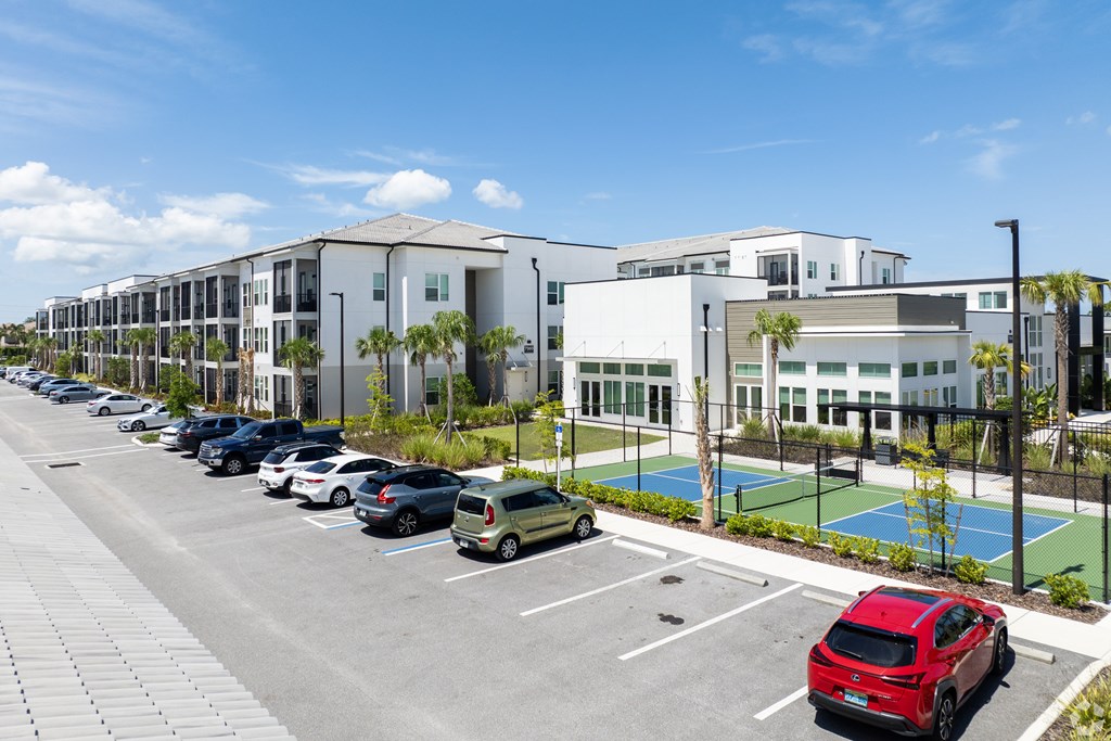 A parking lot with cars and a tennis court in front of a building. at Mira at Palmer Ranch, Sarasota, FL
