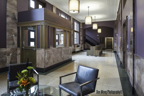 A photograph of a hallway with a black chair and a glass table with flowers on it.