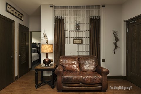 A brown leather couch sits in a room with a lamp and a picture on the wall.