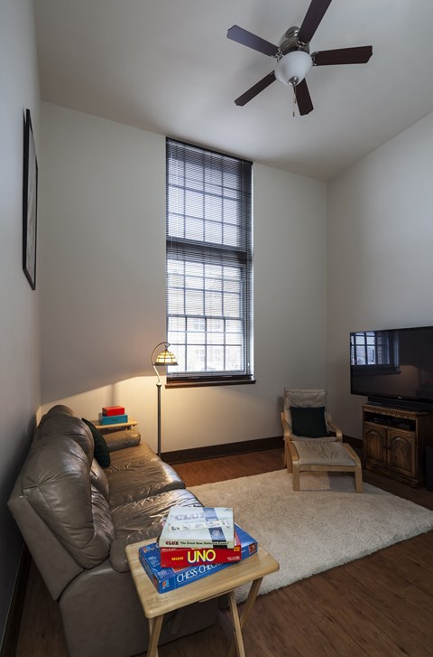 A living room with a couch, a chair, a coffee table, a ceiling fan, and a television.