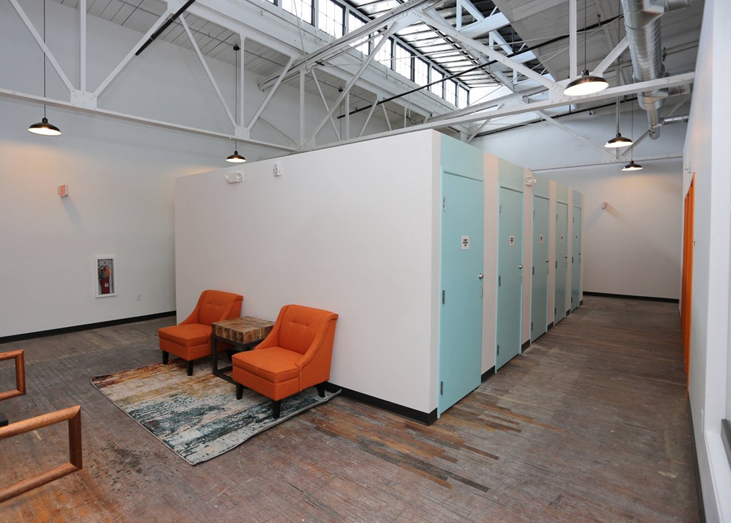 A room with orange chairs and a rug in front of a white wall.