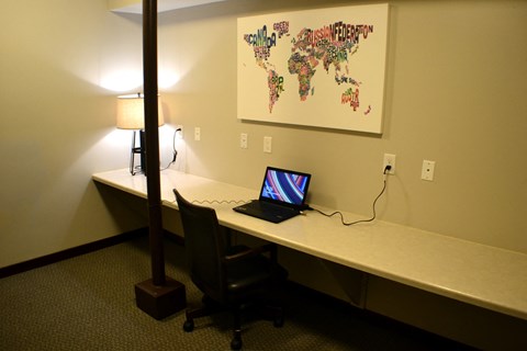 A laptop is on a desk with a world map on the wall behind it.