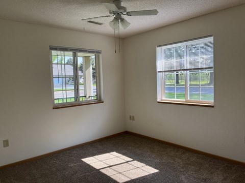 A room with a ceiling fan and two windows.