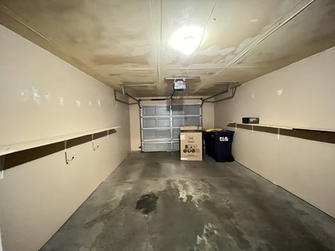A long, narrow, unfinished room with a concrete floor and ceiling, a metal door, and a cardboard box on the floor.