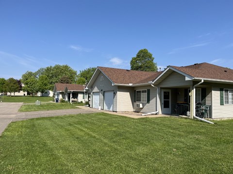 A house with a brown roof and a white door is surrounded by a green lawn.