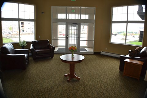 A waiting room with a table in the middle and chairs around it.