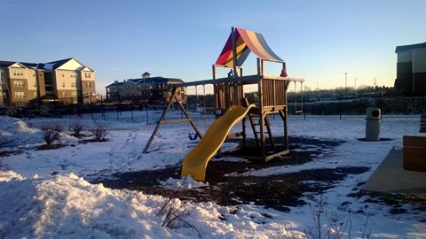 A playground with a yellow slide and a red and yellow umbrella.