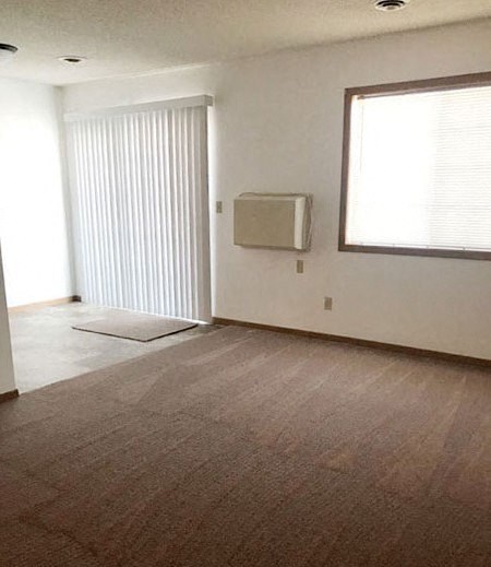 A room with a window, a wall-mounted air conditioner, and a carpeted floor.
