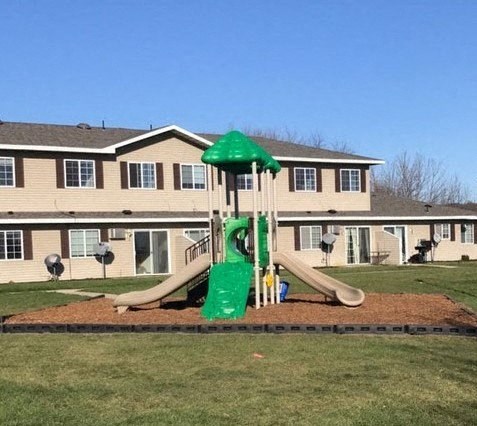 A playground with a green slide in front of a building.