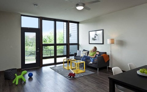 A woman is sitting on a grey couch in a room with a ceiling fan and a framed picture on the wall.