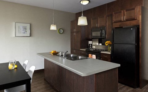 A kitchen with a black refrigerator and a black table with white chairs.