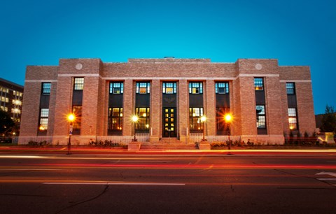 A large brick building with lights on the front and a long exposure of the street in front.