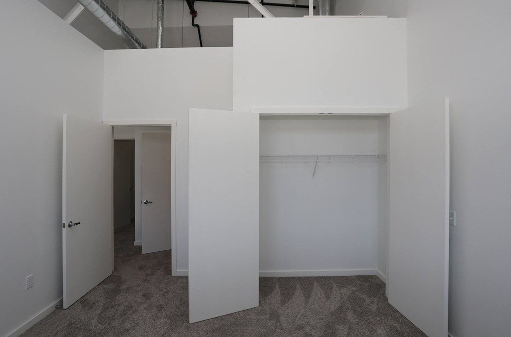 A white room with a carpeted floor and a white ceiling with a pipe.