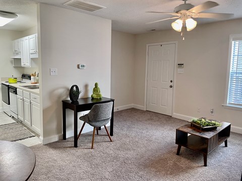 a living room with a ceiling fan and a kitchen in the background
