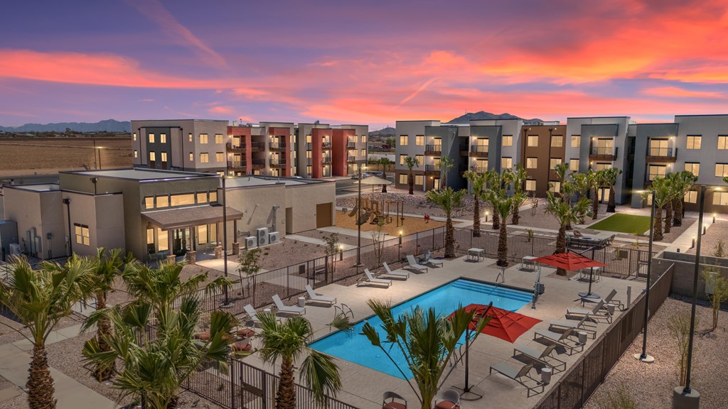 A sunset view of a pool area with palm trees and apartment buildings.