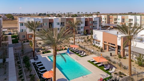 A swimming pool surrounded by palm trees and sun loungers in front of apartment buildings.