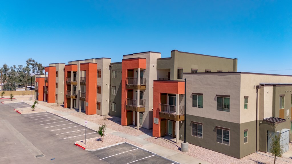 A row of modern apartment buildings with a parking lot in front.