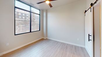 A room with a ceiling fan and a large window overlooking a parking lot.