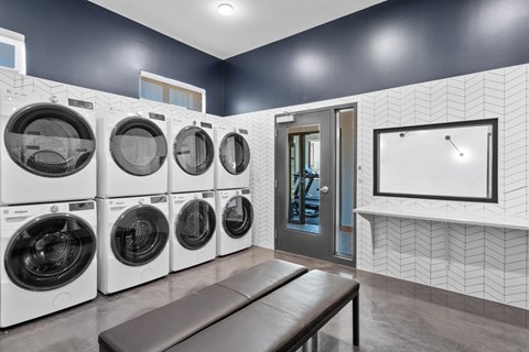 A laundry room with a row of washing machines and a bench.