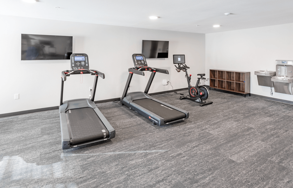 two treadmills and exercise bikes in a gym with a tv