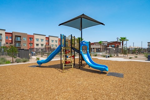 A playground with a blue slide and a black umbrella.