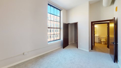 A room with a carpeted floor and a window with a view of a building outside.