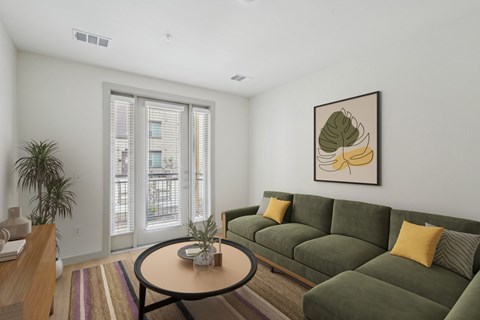 A living room with a green couch and a framed picture of a plant on the wall.