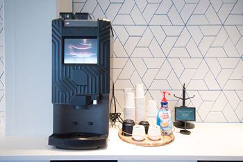 a coffee maker on a counter next to a shelf with coffee cups and a bottle