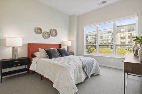 A bedroom with a bed, nightstand, and a window overlooking a building.
