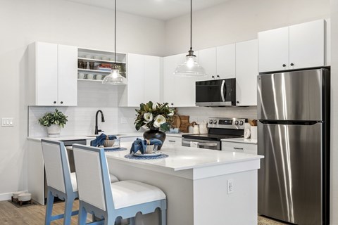 A modern kitchen with a stainless steel refrigerator, white cabinets, and a center island with a sink and dining table.