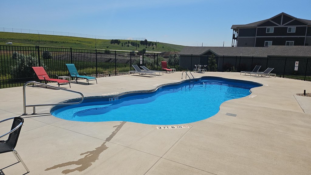 a swimming pool with chairs and a building in the background