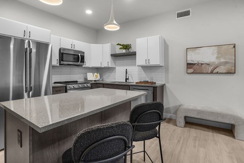 A kitchen with a refrigerator, microwave, and a counter with a chair.