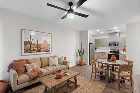 A living room with a couch, a coffee table, a dining table, and a ceiling fan.