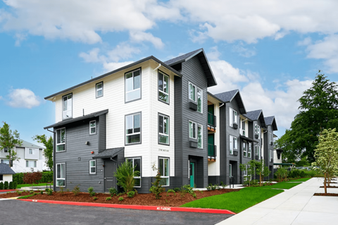 A modern apartment building with grey and white exterior and red mulch in the front yard.