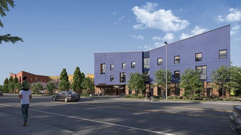 A man is walking on the street in front of a purple building.