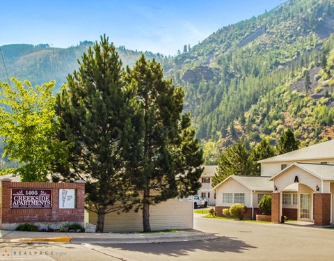 A sign for Creekside Apartments is in front of a building with a mountain in the background.