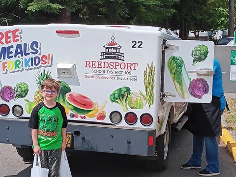 A truck with a Reedsport school district logo and a sign that says "Free Meals for Kids!" is parked in a parking lot.