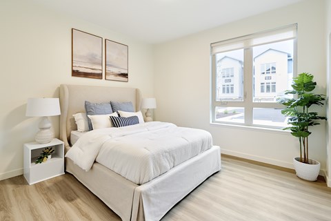 A bedroom with a large bed, two lamps, and a potted plant.