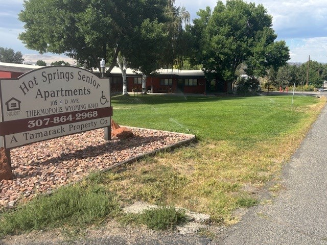 A sign for Hot Springs Senior Apartments is in front of a grassy area.