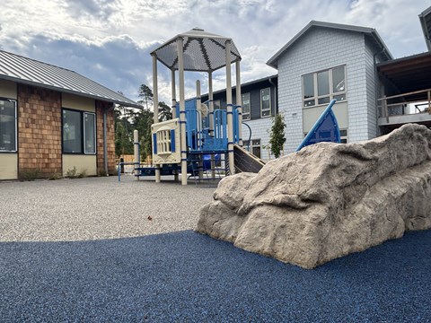 A playground with a large rock in the foreground and a swing set in the background.