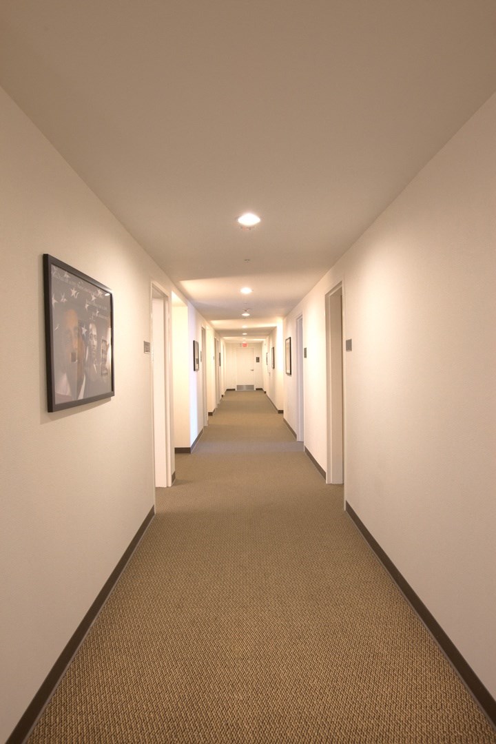 a long hallway with white walls and brown carpeting and a picture on the wall