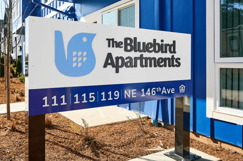 A sign for The Bluebird Apartments is displayed in front of a building.