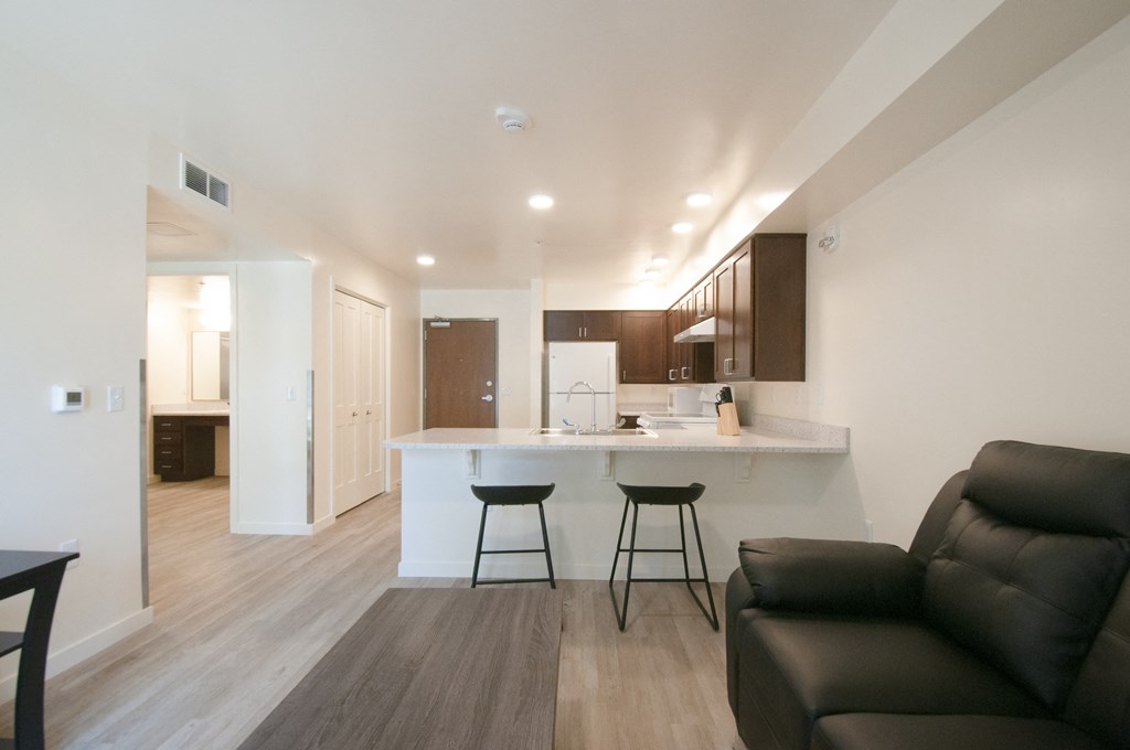a living room with a couch and a kitchen with a bar and stools
