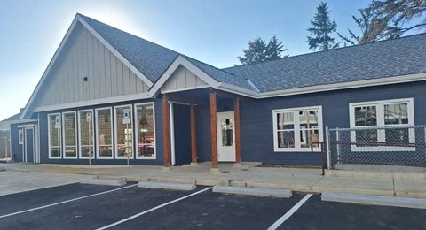 A building with a grey roof and blue walls with a parking lot in front.