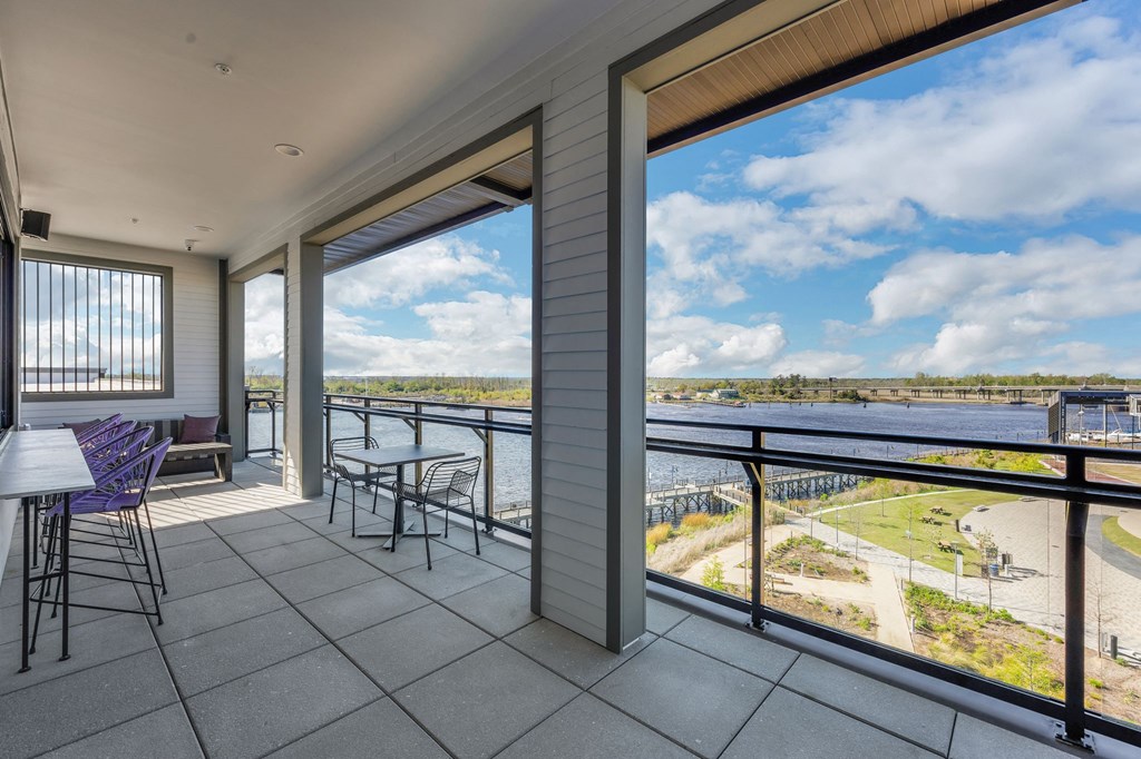 a balcony with a view of a river and a patio with tables and chairs at Metropolitan at the Riverwalk, Wilmington, NC