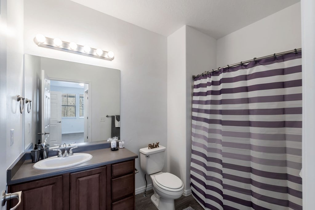 A bathroom with a sink, toilet, and striped shower curtain.at Florentine Villas, Midvale, 84047