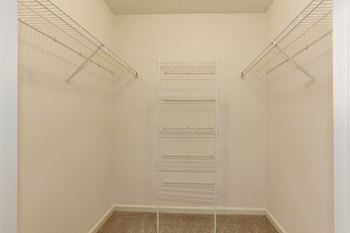 a walk in closet with four metal shelves in a white room at County Center Crossing Apartments in Woodbridge, VA