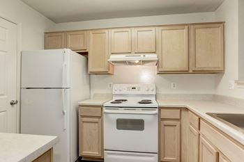 an empty kitchen with white appliances and wooden cabinets at County Center Crossing Apartments in Woodbridge, VA