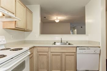 a kitchen with white appliances and wooden cabinets at County Center Crossing Apartments in Woodbridge, VA